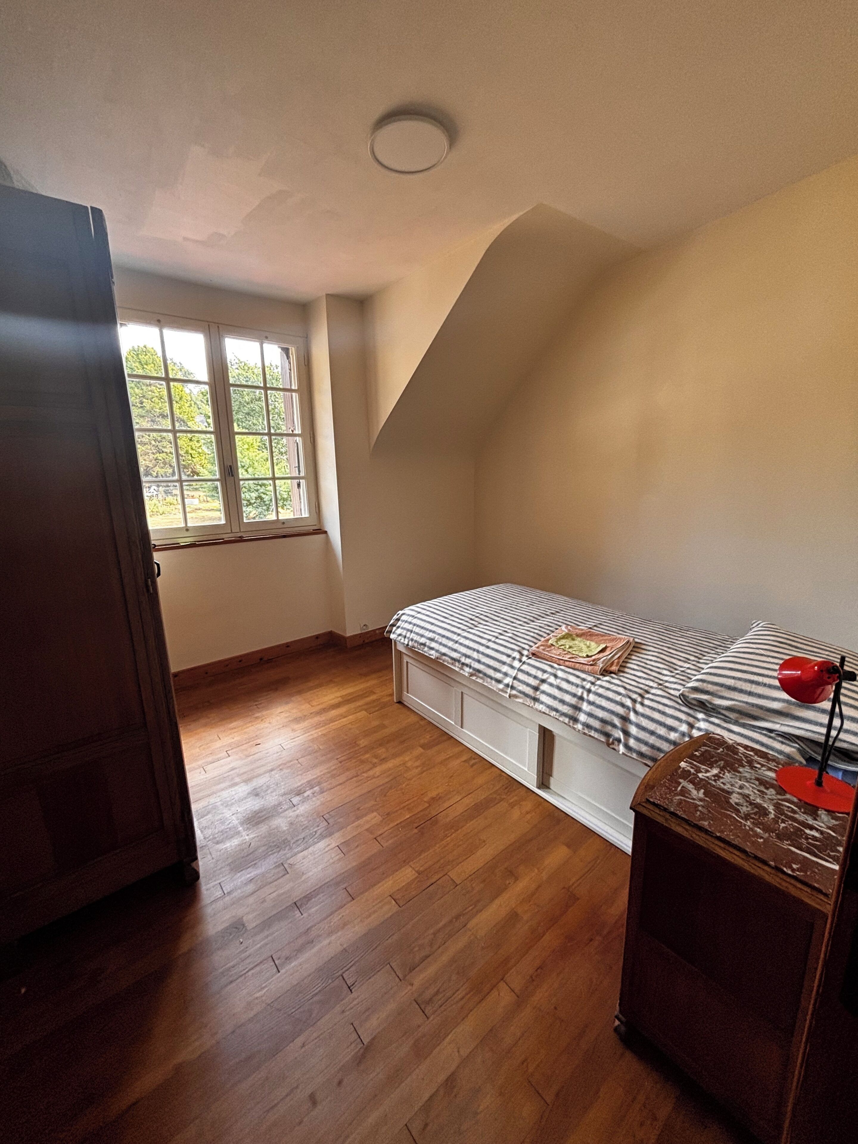 Een slaapkamer met een bed, een raam en een houten vloer.