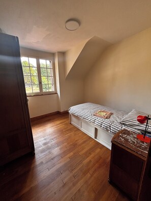 A bedroom with a bed, a window, and a wooden floor. - 600 meters from the beach, a former farmhouse that sleeps 5; pets allowed. (Erquy)