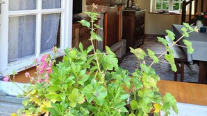 A room with a stone fireplace, wooden beams, a dining area, and potted plants.