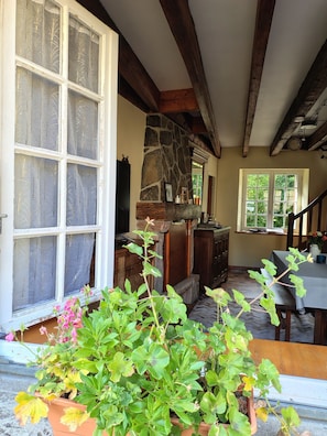 A room with a stone fireplace, wooden beams, a dining area, and potted plants.