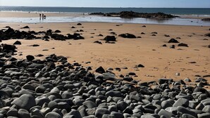 A beach with a rocky foreground and a clear sky.