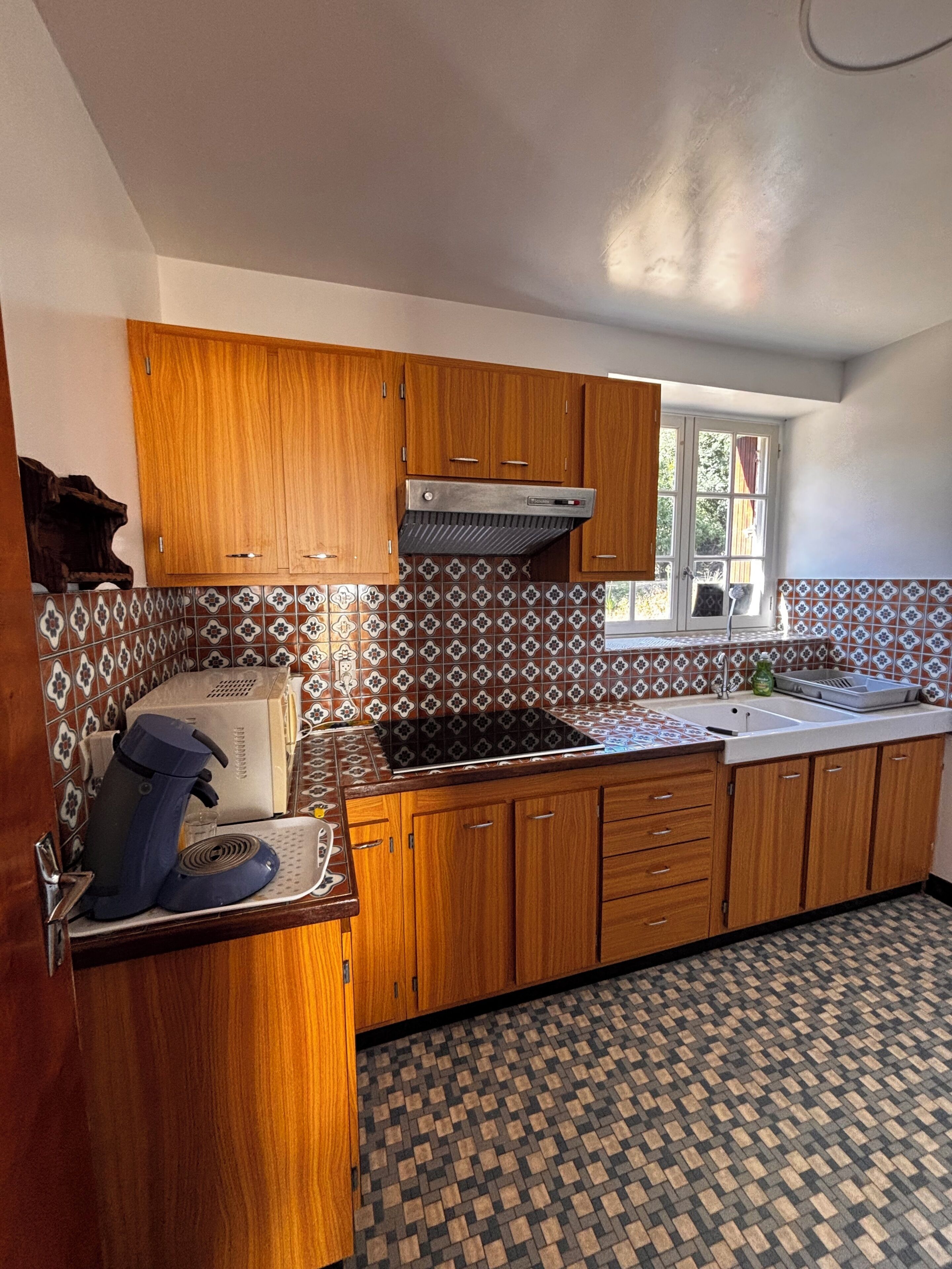 Een keuken met houten kastjes, een ingebouwde kookplaat en een betegelde spatwand.