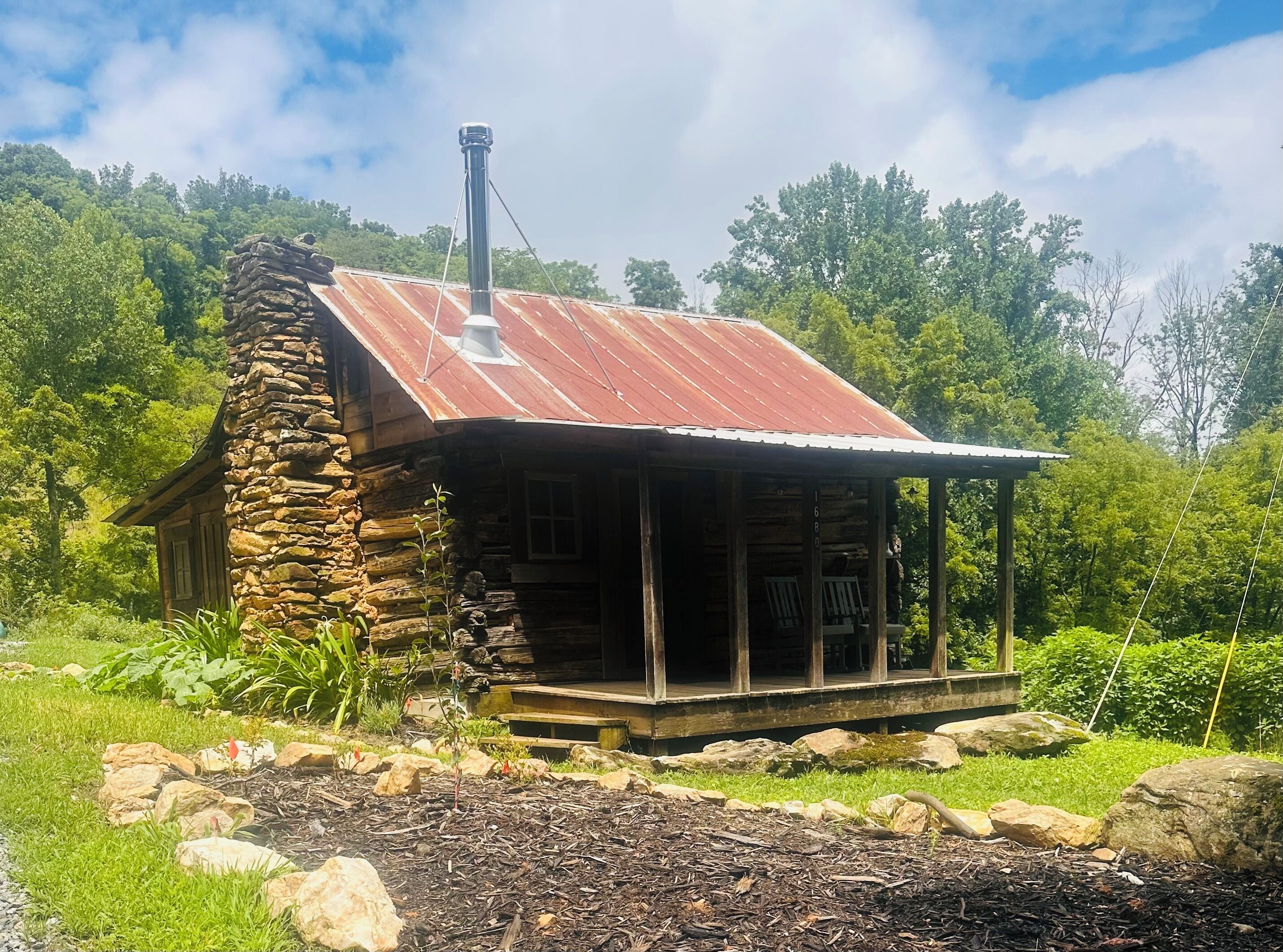 A rustic cabin with a stone chimney, wooden porch, and a metal roof.