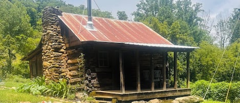 A rustic cabin with a stone chimney, wooden porch, and a metal roof.