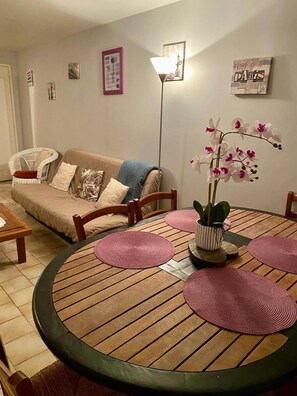 A living room with a round wooden table, a sofa, and a floor lamp. - Gîte "Le Petit Clos" (Amboise)