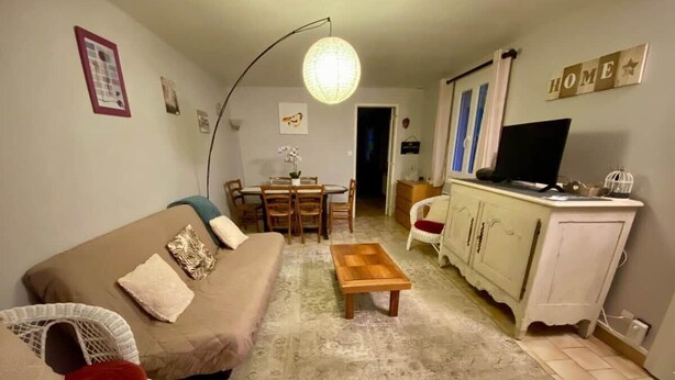 Ett vardagsrum med en soffa, ett soffbord, ett matbord med stolar, en tv och ett skåp.
