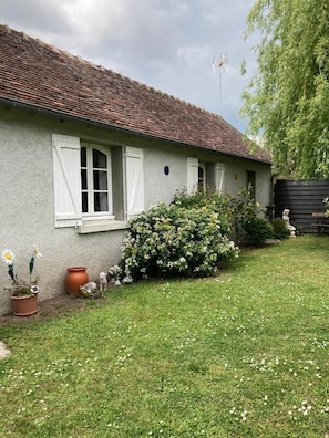 A house with a tiled roof, white window shutters, and a garden with flowers and a small statue. - Gîte "Le Petit Clos" (Amboise)