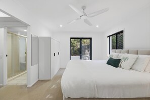 Ein Schlafzimmer mit einem Bett, einem Deckenventilator, einem Fenster und einer Tür zu einem Badezimmer.