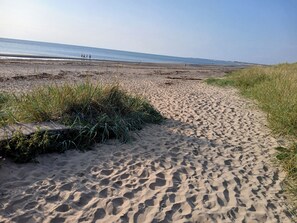 A sandy beach path leading to the ocean with footprints and grass on the sides. - Apartment Sleeps 4 With Garden (Prestwick)