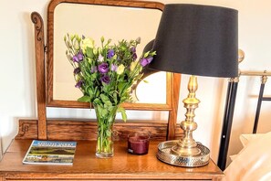 A wooden nightstand with a mirror, a lamp, a candle, and a book. - Apartment Sleeps 4 With Garden (Prestwick)