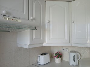A kitchen with white cabinets, a toaster, a kettle, and a flower vase on the countertop. - Apartment Sleeps 4 With Garden (Prestwick)