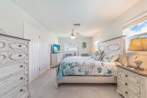 Un dormitorio con cama, cómoda, televisor y ventilador de techo.