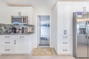 Eine moderne Küche mit weißen Schränken, einer eingebauten Mikrowelle, einer Kaffeemaschine und einem Kühlschrank.