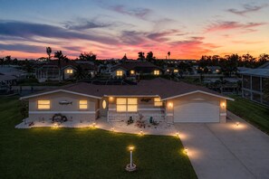 Uma casa com garagem, um jardim bem iluminado e um céu ao entardecer.