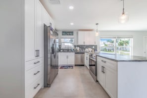 A modern kitchen with white cabinetry, stainless steel appliances, and a large window offering a view of the outdoors. - Ga1970 3 Bedroom Home (Englewood)