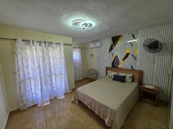 A bedroom with a bed, curtains, a fan, and a wall with abstract art.