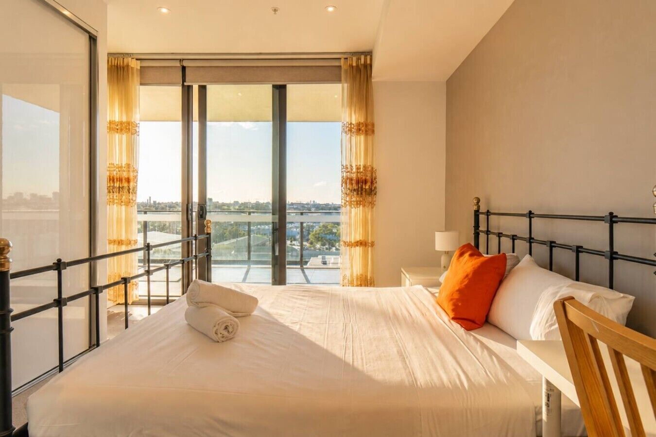 Une chambre d’hôtel avec un grand lit, une table de chevet, une lampe et une vue sur le paysage urbain grâce à de grandes fenêtres du sol au plafond.