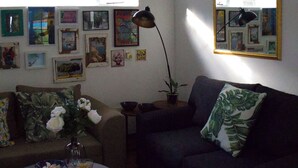 A living room with a sofa, a coffee table, and a lamp. There are framed pictures on the wall. - Lemon Tree Cottage..a little piece of heaven (Johannesburg)