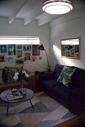 Ein Wohnzimmer mit einer Couch, einem Couchtisch und einer Lampe. An der Wand hängen gerahmte Bilder.