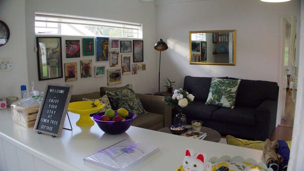 A living room with a sofa, a coffee table, a bowl of fruit, and a sign on the counter. - Lemon Tree Cottage..a little piece of heaven (Johannesburg)