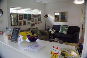 Uma sala de estar com sofá, mesa de centro, uma cesta de frutas e um aviso no balcão.