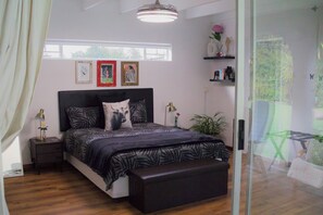Ein Schlafzimmer mit einem Bett, Nachttischen, einem Fenster und Blick ins Grüne.
