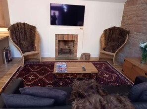 A living room with two armchairs, a sofa, a fireplace, a television, and a rug. - Holiday Cottage Sleeps 3 With Garden (Prestwick)