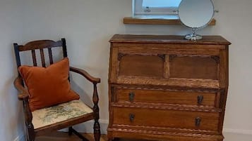 A wooden dresser with drawers and a mirror, a wooden chair with a cushion, and a window above the dresser.