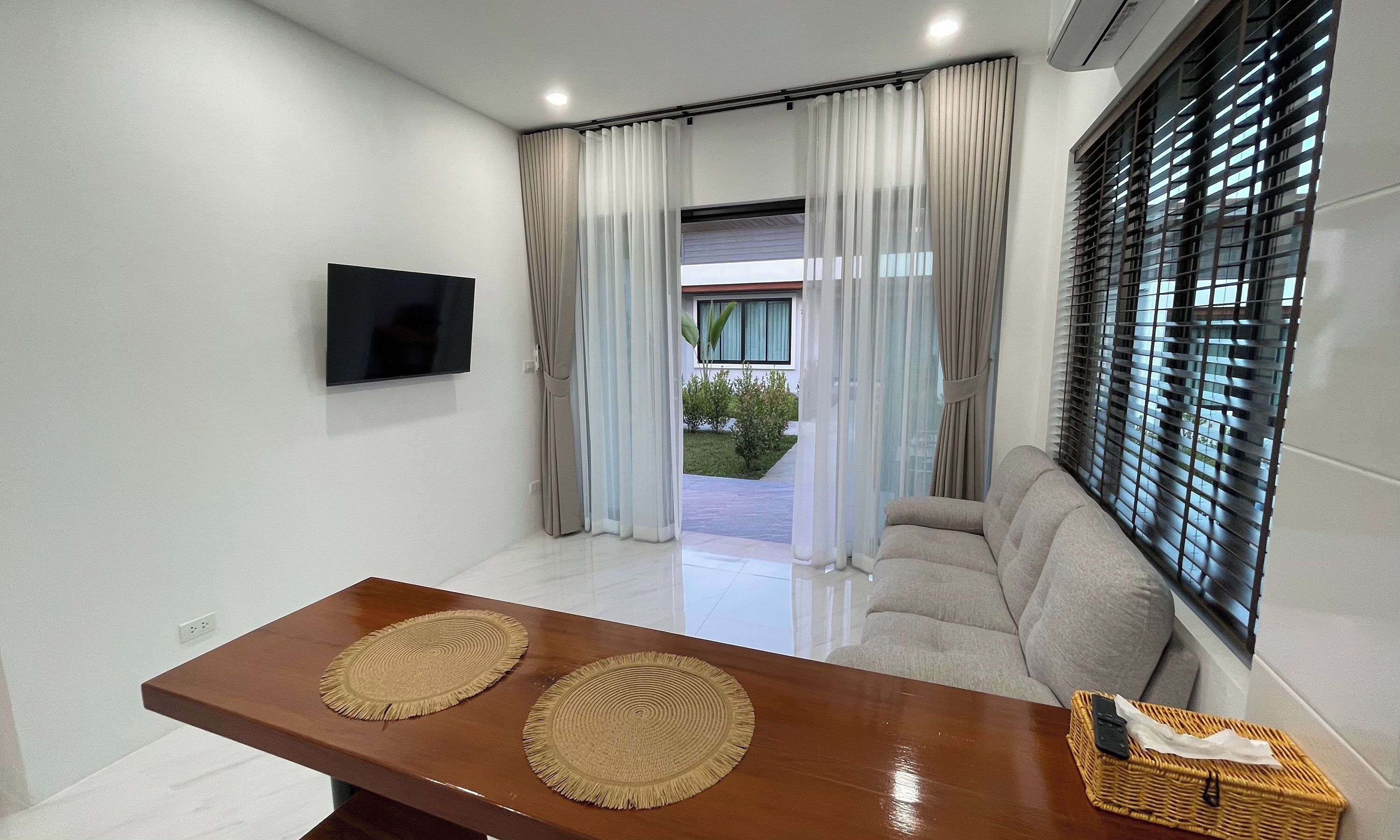 A modern living room with a sofa, a TV mounted on the wall, and a wooden table with two woven placemats.