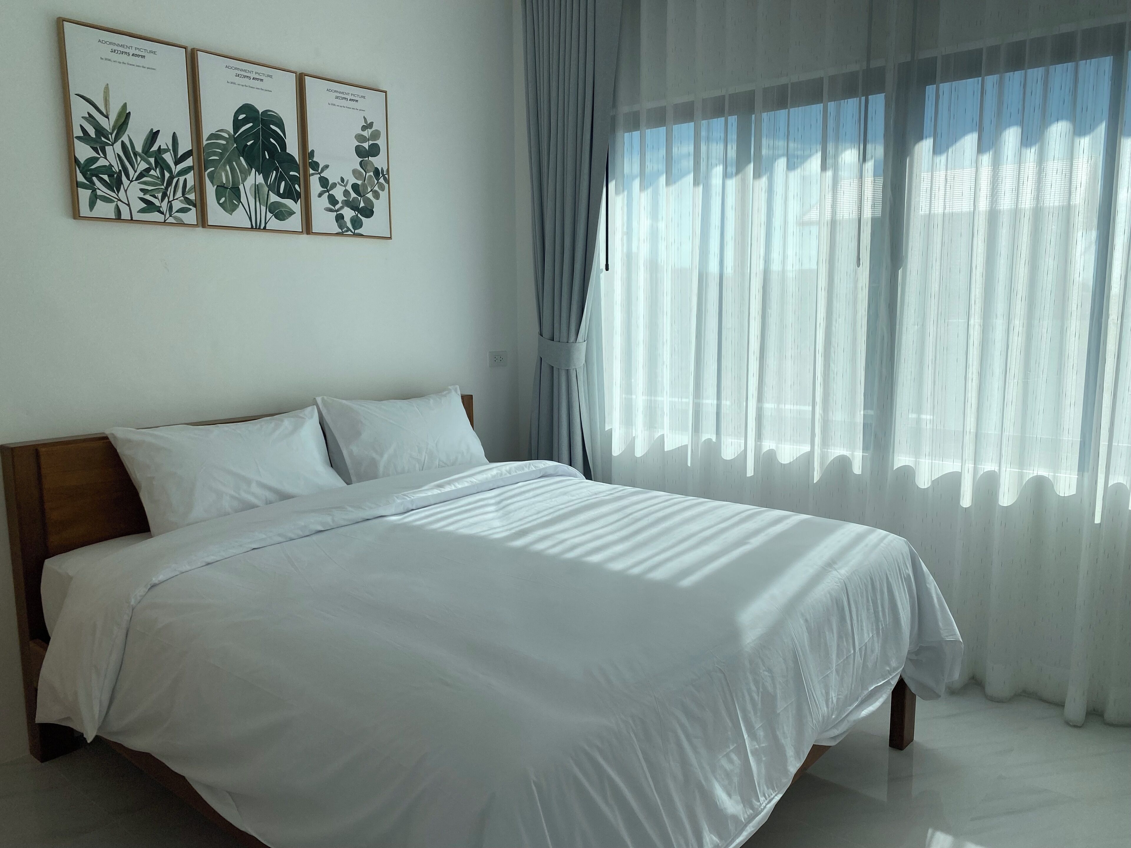 A bedroom with a large bed, white bedding, and three framed botanical prints on the wall.