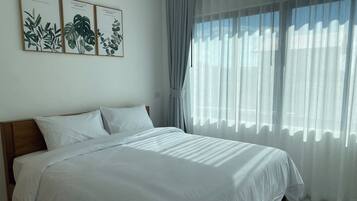 A bedroom with a large bed, white bedding, and three framed botanical prints on the wall.