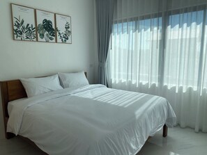 Un dormitorio con una cama grande, ropa de cama blanca y tres láminas botánicas enmarcadas en la pared.