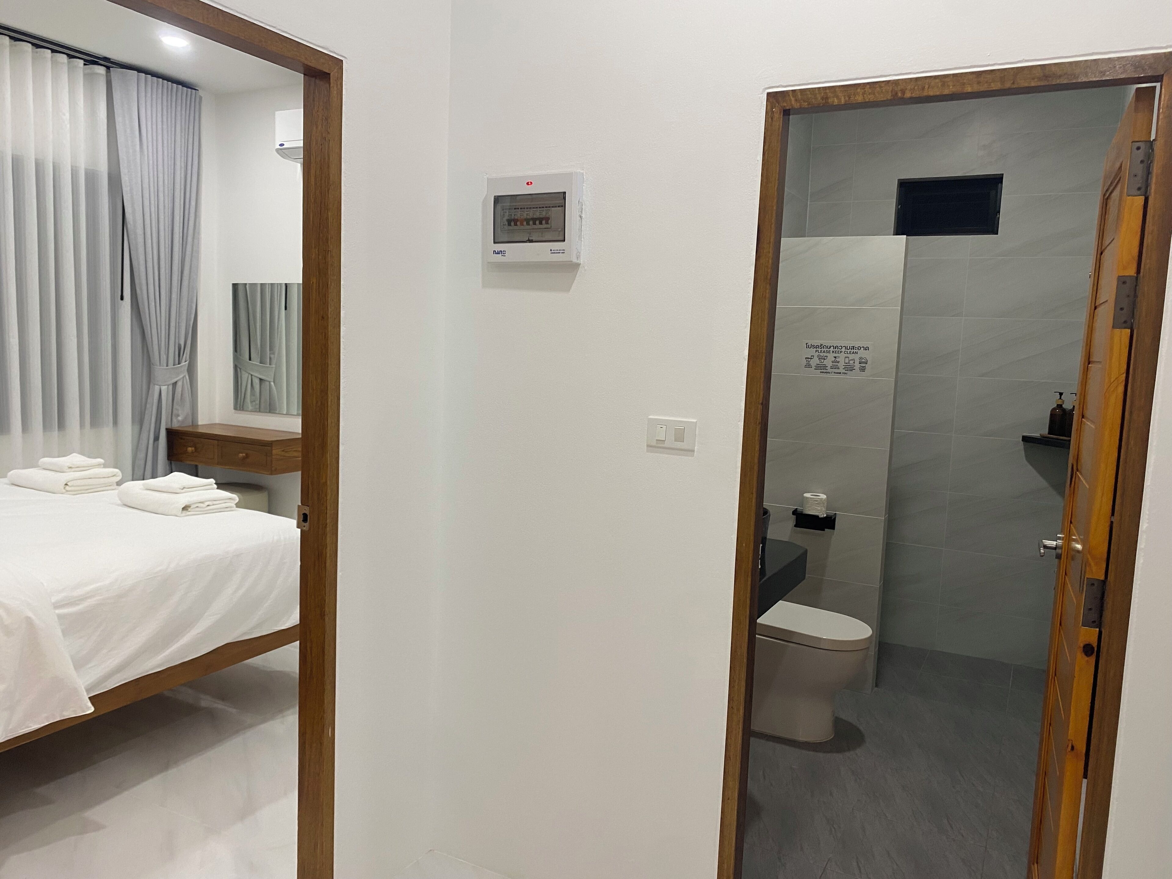 A hotel room with a bed, a bedside table, a mirror, a wall-mounted air conditioning unit, and a shower area with a toilet.