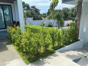 Un área exterior moderna con un sendero de hormigón, setos bien cuidados y un césped.