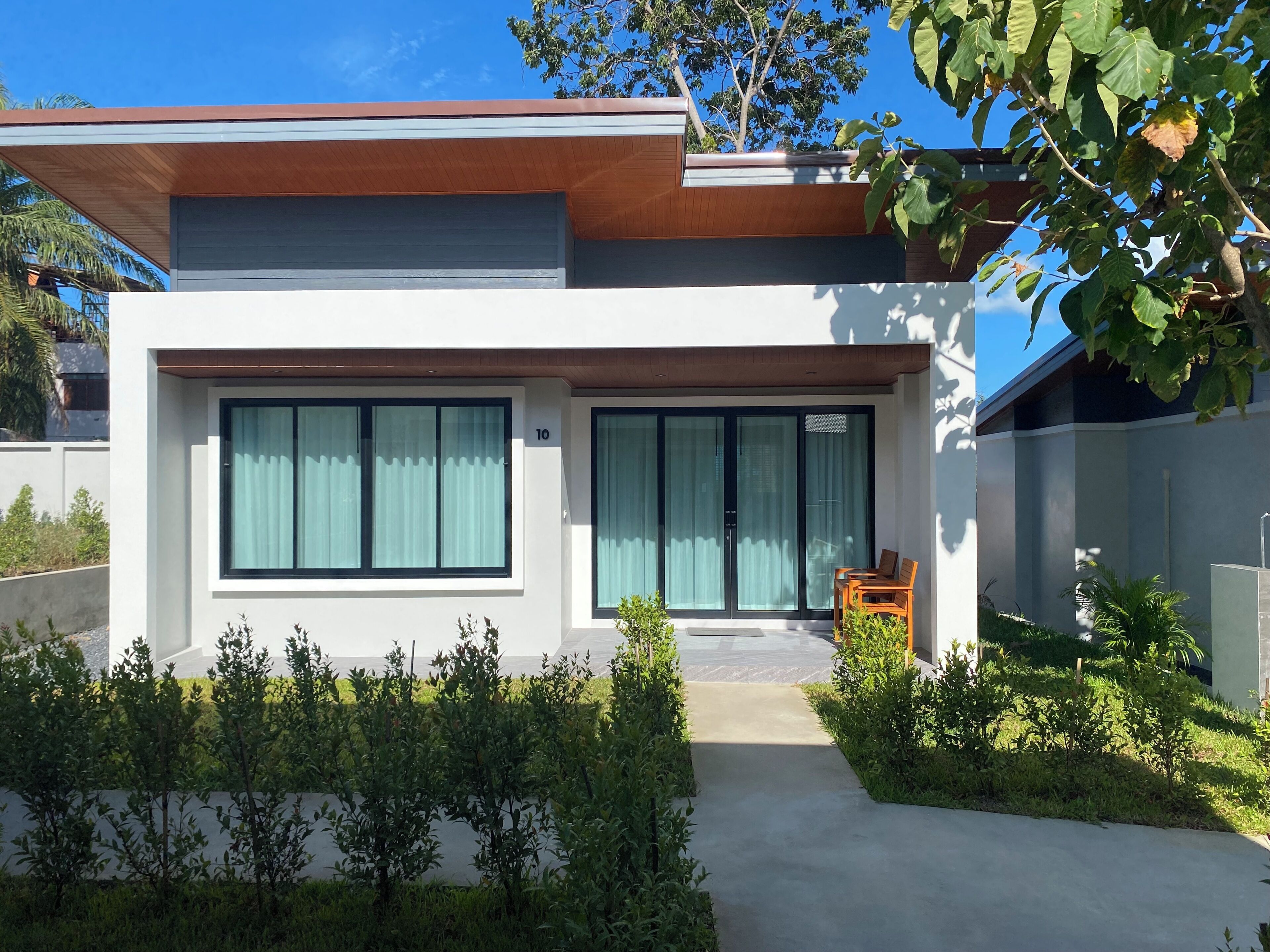 A modern two-story house with large windows, a visible number '10', and a small outdoor seating area.
