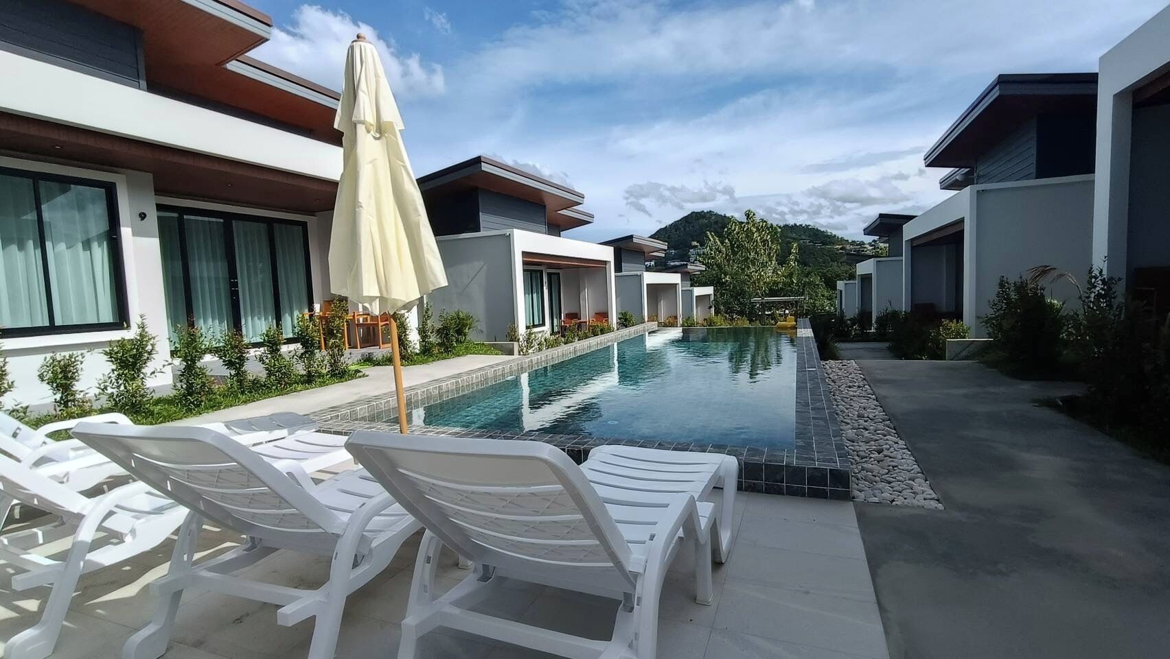 Un hôtel moderne doté d’une piscine, de chaises longues blanches et d’un parasol.