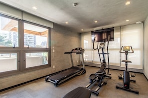 A gym with a treadmill, elliptical, and weight machine, large windows, and a TV on the wall. - Studio Premium - 2 Blocks from NuBank Park (São Paulo)
