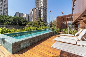 A rooftop pool area with a wooden deck, lounge chairs, and a view of surrounding high-rise buildings. - Studio Premium - 2 Blocks from NuBank Park (São Paulo)