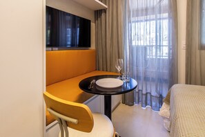A compact hotel room with a single bed, a small table with a white plate, a glass, and cutlery, and a window with curtains. - Studio Premium - 2 Blocks from NuBank Park (São Paulo)