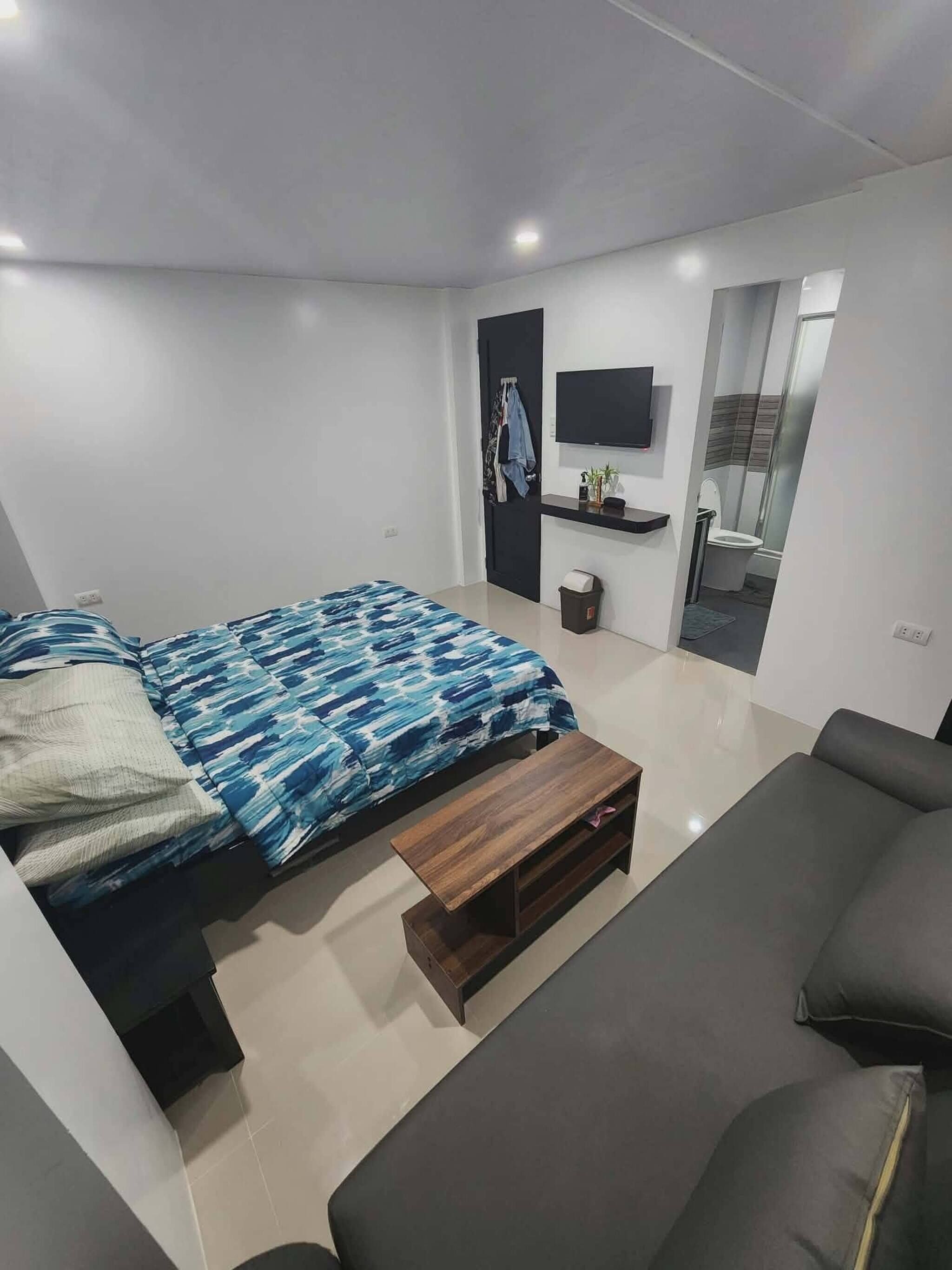 A modern bedroom with a bed, a sofa, a TV, and a small table.