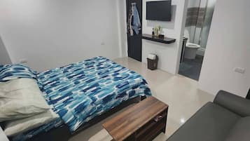 A modern bedroom with a bed, a sofa, a TV, and a small table.