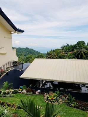A house with a large covered patio, surrounded by lush greenery and a view of distant hills. - Avana Hills Tagaytay Manor - London (Tagaytay)