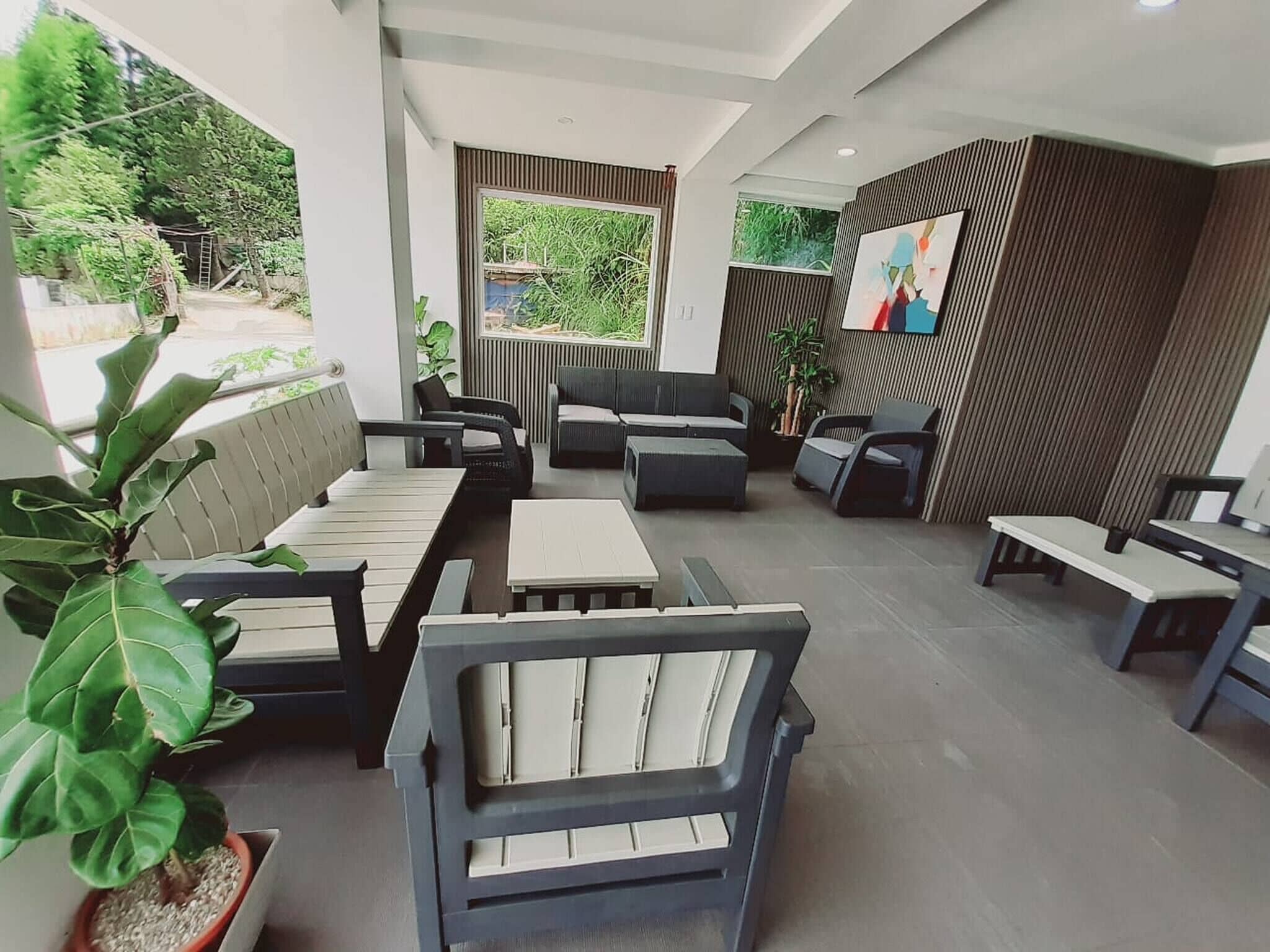 Un espace extérieur moderne aménagé avec des canapés et des tables, entouré de plantes et d’un mur en bois.