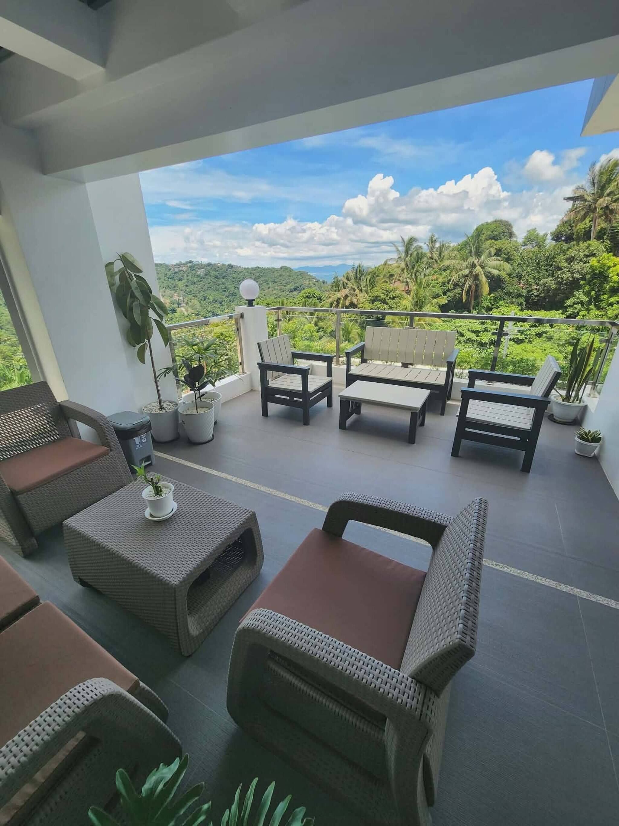 A balcony with wicker furniture, potted plants, and a view of a lush landscape.