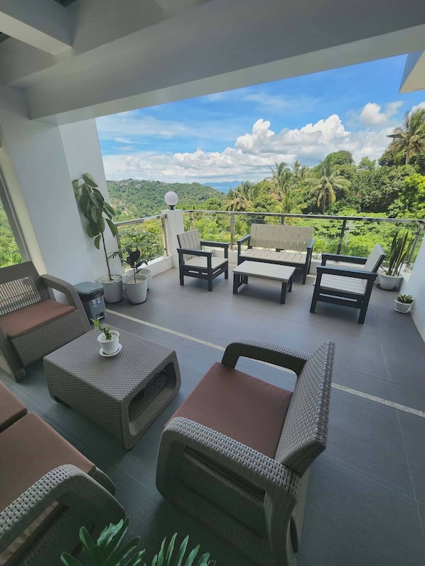 A balcony with wicker furniture, potted plants, and a view of a lush landscape.