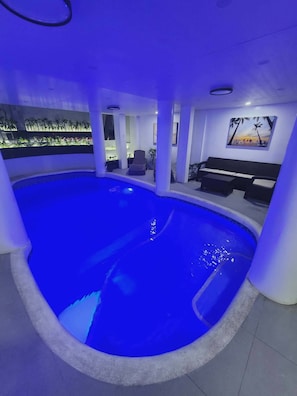 An indoor swimming pool with a blue hue, surrounded by a white interior, and a seating area with a view of the pool. - Avana Hills Tagaytay Manor - London (Tagaytay)