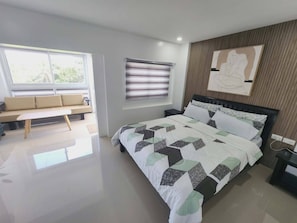A modern bedroom with a bed, a bench, a window with blinds, and a wall-mounted artwork. - Avana Hills Tagaytay Manor - London (Tagaytay)