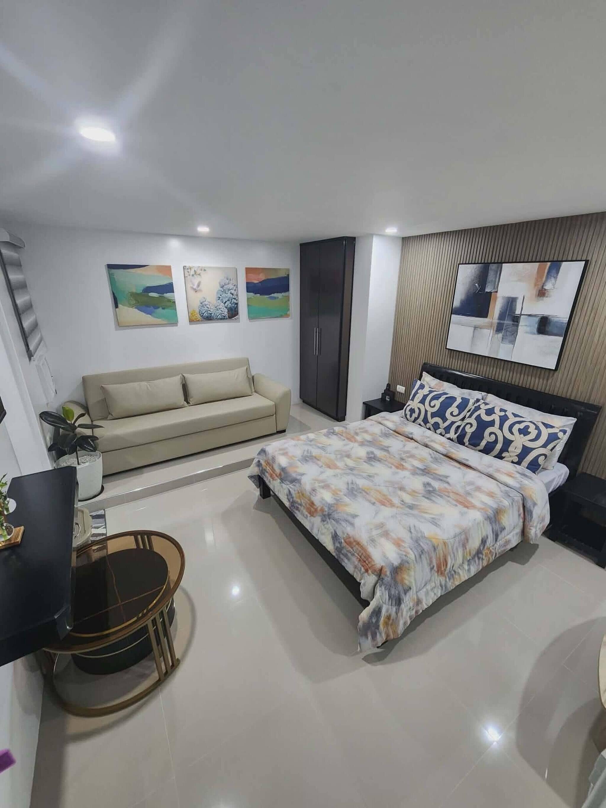 Une chambre à coucher moderne avec un lit, un canapé, un téléviseur et des œuvres d’art accrochées aux murs.