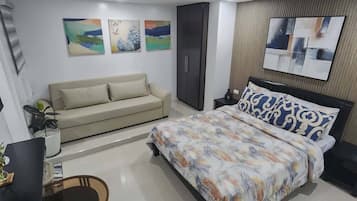 Une chambre à coucher moderne avec un lit, un canapé, un téléviseur et des œuvres d’art accrochées aux murs.