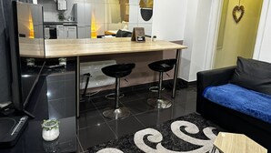A modern kitchen with a central island, two bar stools, a black sofa, and a small coffee table. - Walk to Stadium and City Center (Cardiff)